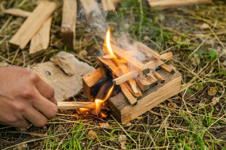 A close-up view of a fire being lit using firewood kindling outdoors.